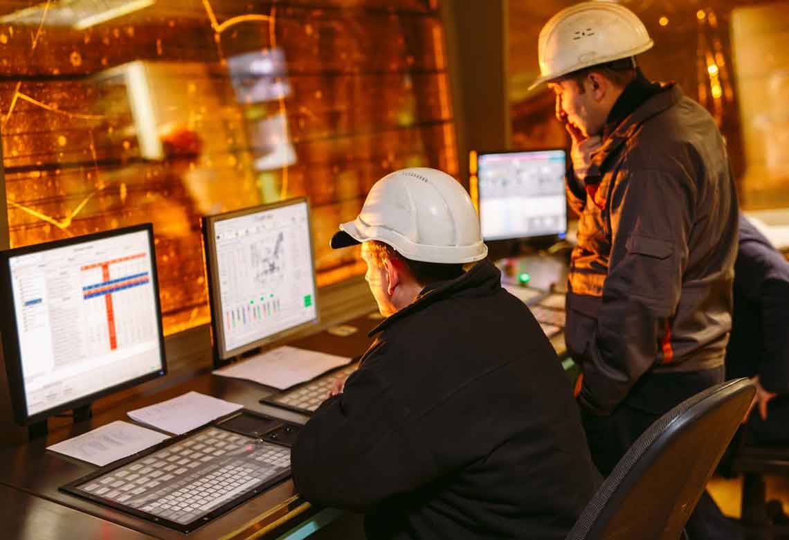 Two men in hard hats looking at technical screens