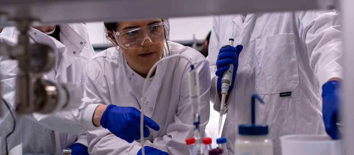 Close up of three researcher in lab coats holding a sharp instrument