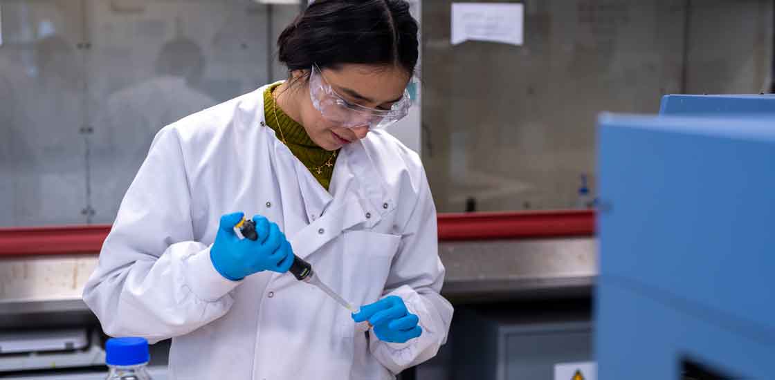 Person in a lab coat injecting a tube with black liquid.