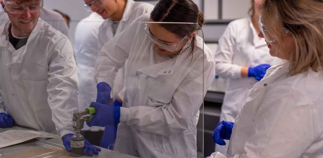 researcher in a lab holding metal tool over a small bottle filled with black liquid